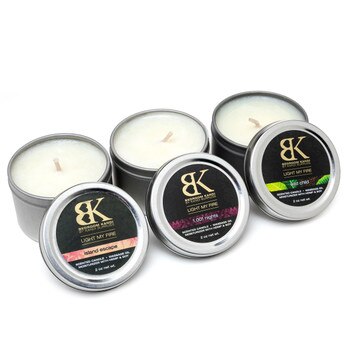 An image of three small massage oil candle tins in a row with their lids propped up in front of them, displaying the fragrances.